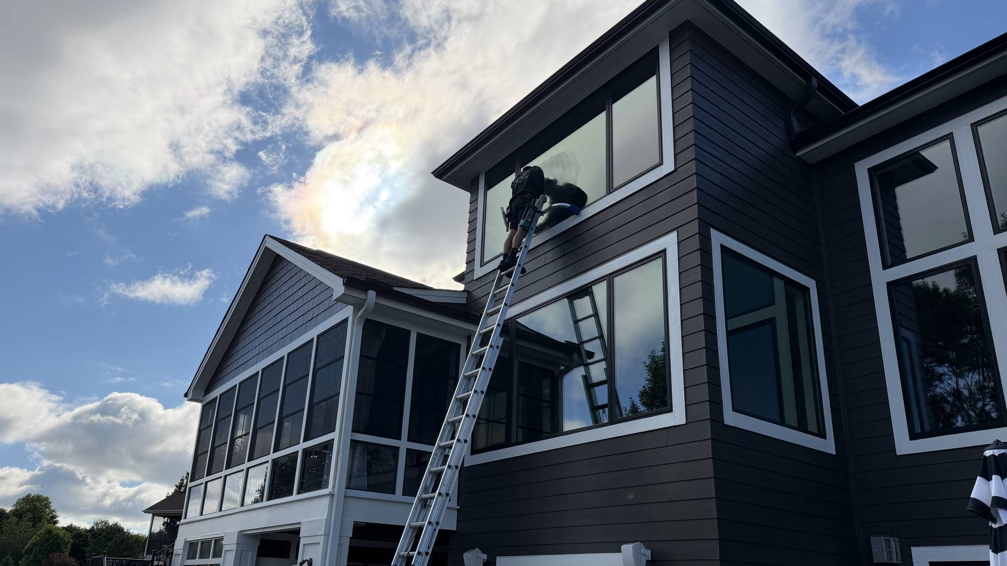 A Strongman Window Cleaning technician on a ladder cleaning second-story windows on a Woodbury home